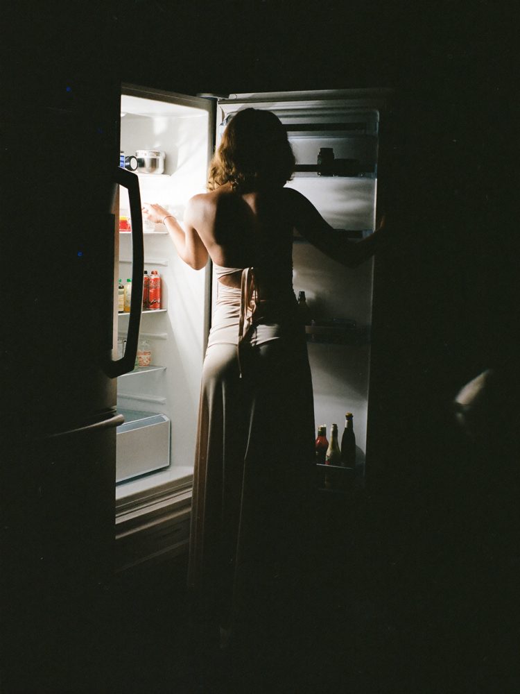 A woman at an open fridge at 1am in a dark kitchen